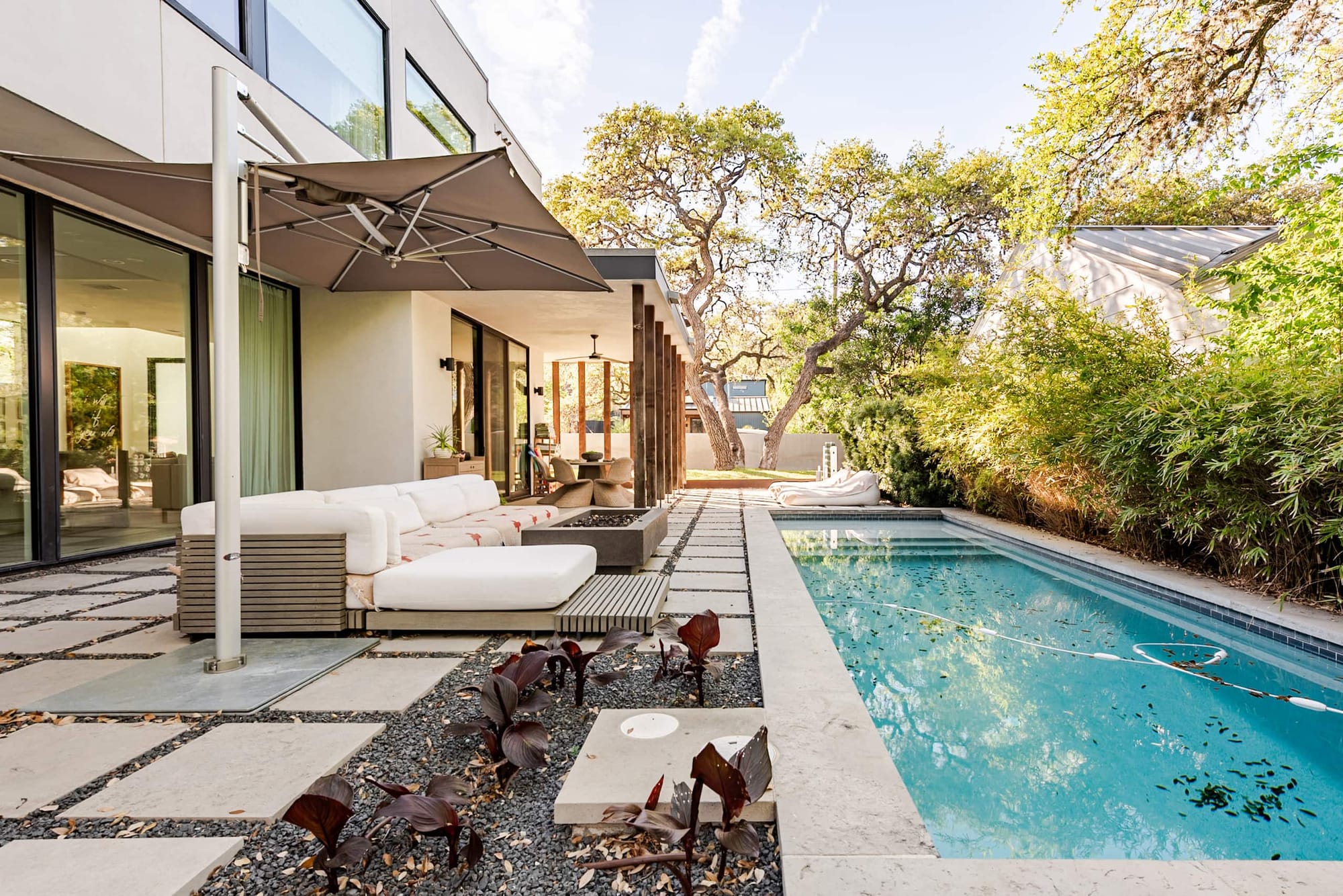 The courtyard at Bali in Bouldin — a white outdoor sofa and sculptural plantings between stone pavers, along the length of the pool