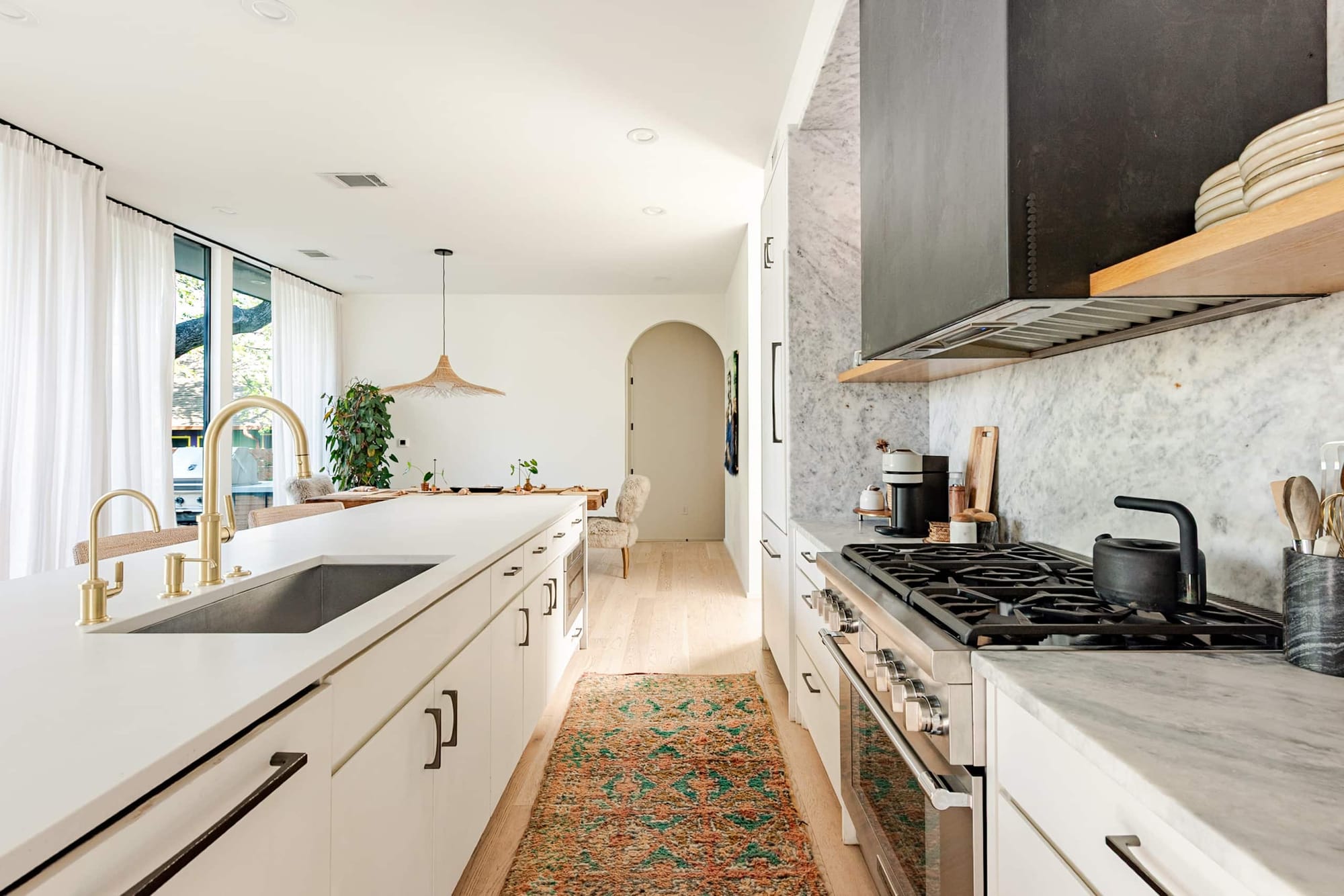 The kitchen — brass faucet, marble backsplash, black range hood, and a vintage runner adding golden color underfoot
