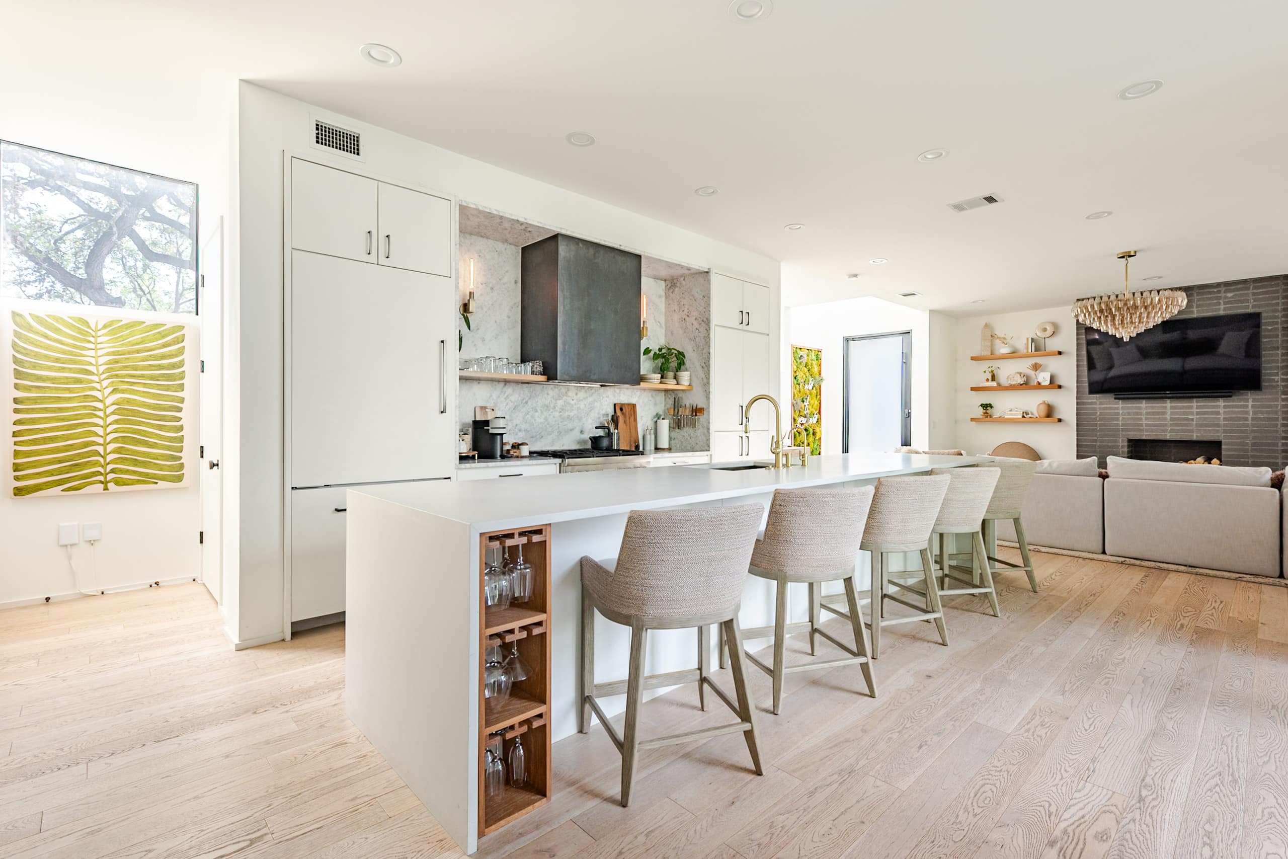 The kitchen — a white waterfall island with linen counter stools, built-in wine storage, and wide-plank oak floors