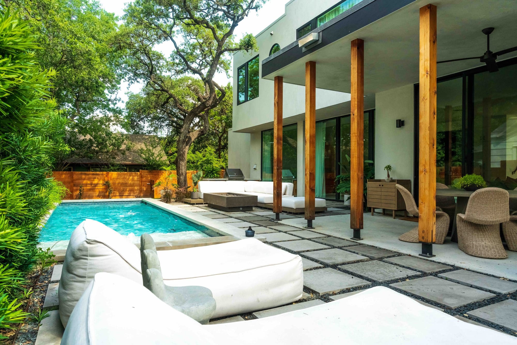 Poolside at Bali in Bouldin — white chaise loungers by the water, cedar columns, and the two-story home beyond