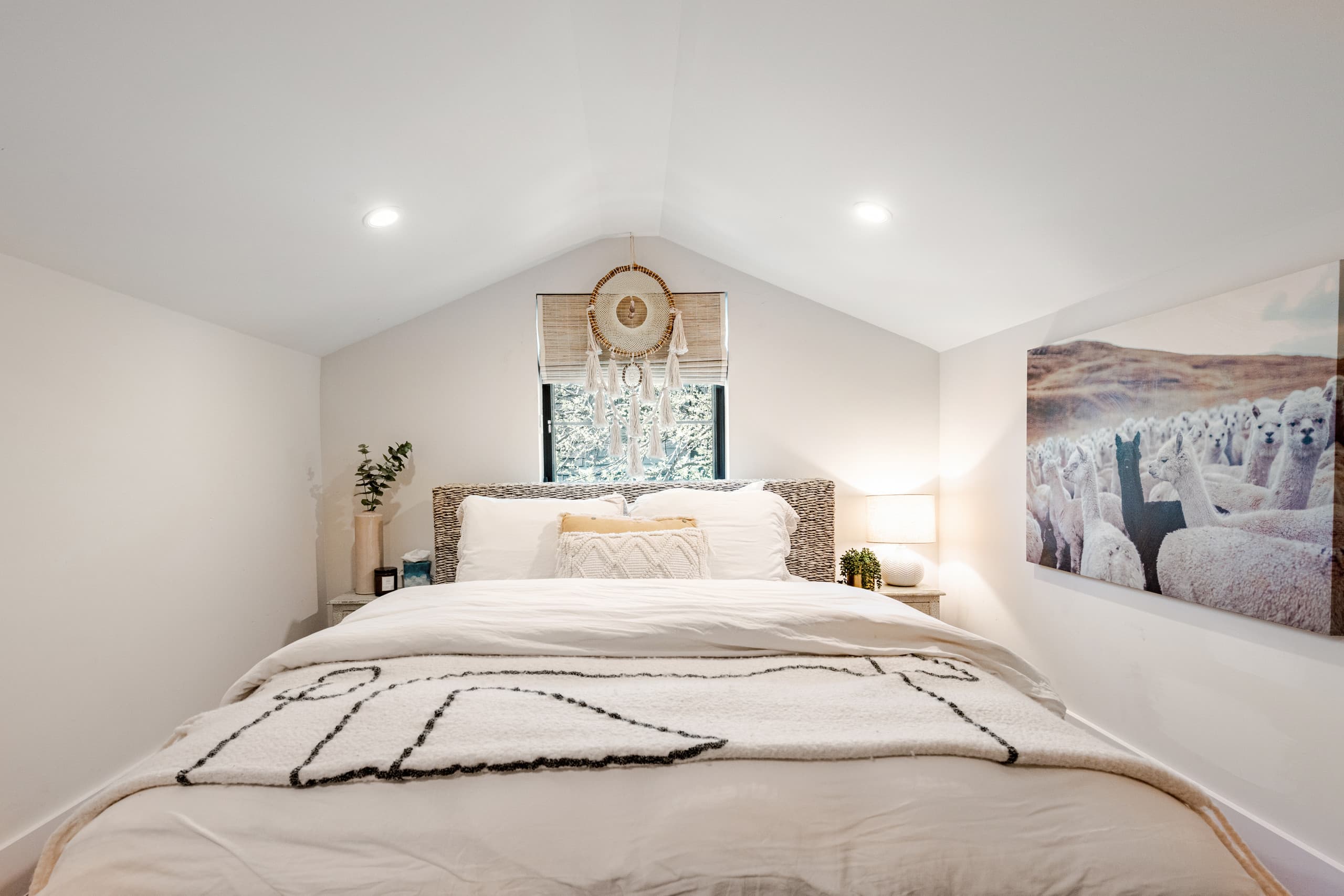 A guest bedroom — an alpaca art print beside the bed under a vaulted ceiling, a woven dreamcatcher above the window