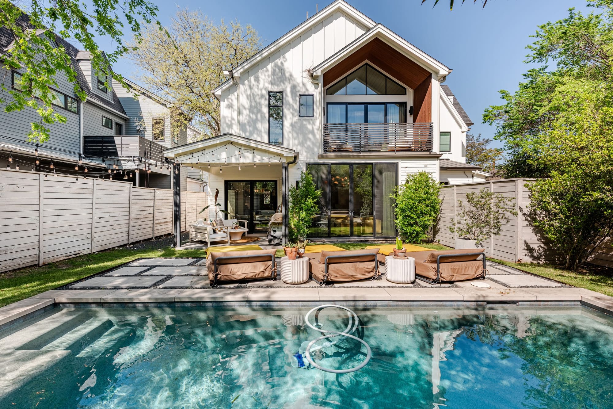 The Hether Haus from the back garden — a modern farmhouse with board-and-batten siding and a wood gable, pool and loungers in the foreground