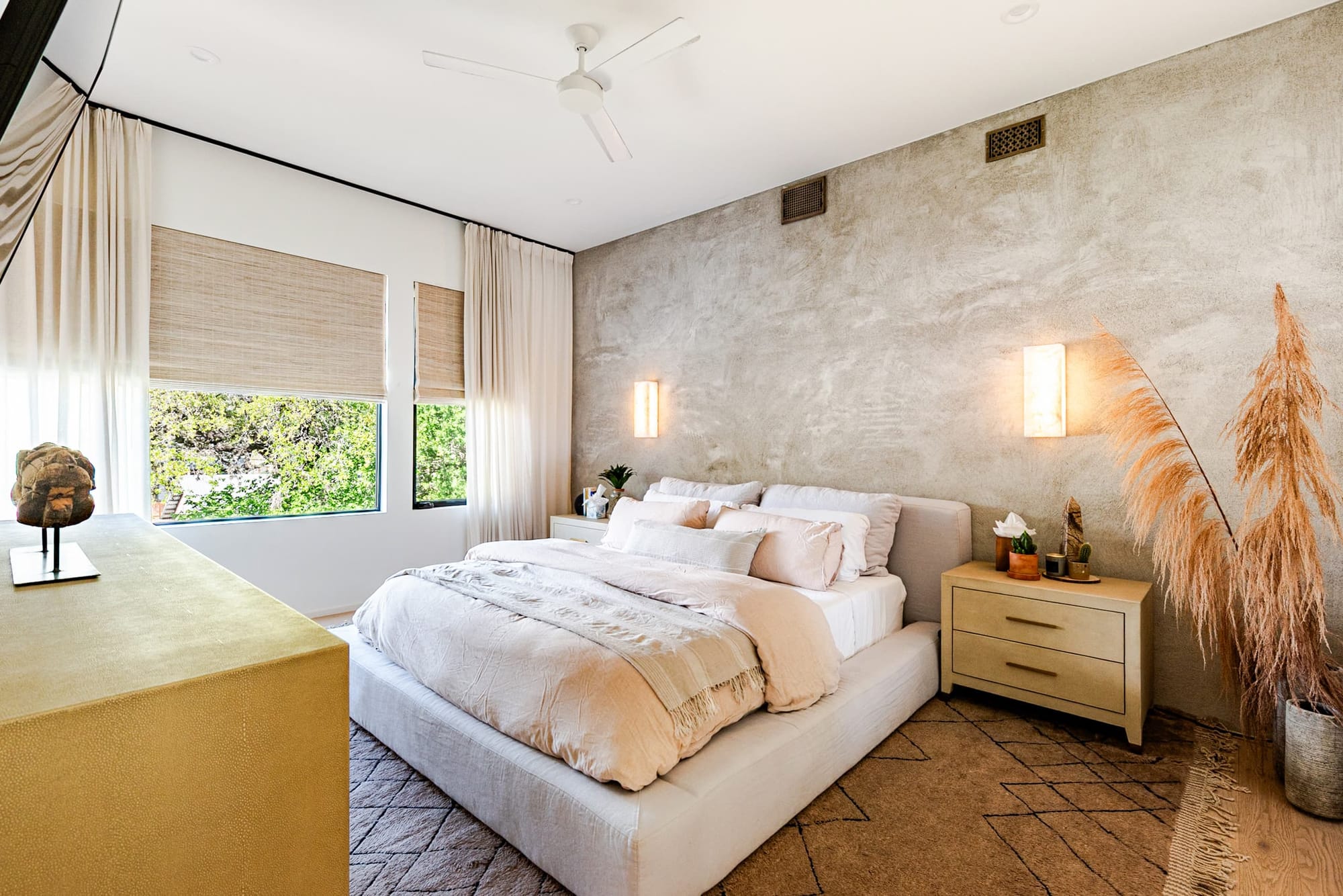 A guest bedroom with a limewash plaster feature wall, warm sconce light, pampas grass, and layered cream linens