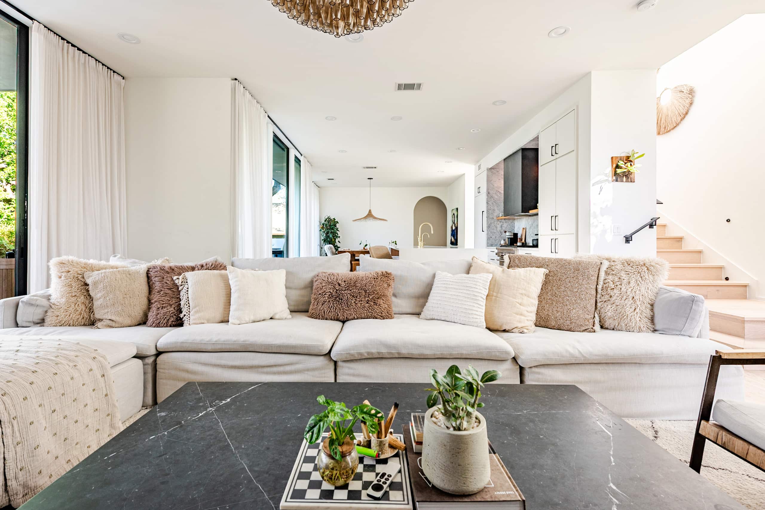 The great room at Bali in Bouldin — a deep cream sectional beneath a tiered brass chandelier, open to the kitchen and the stair beyond